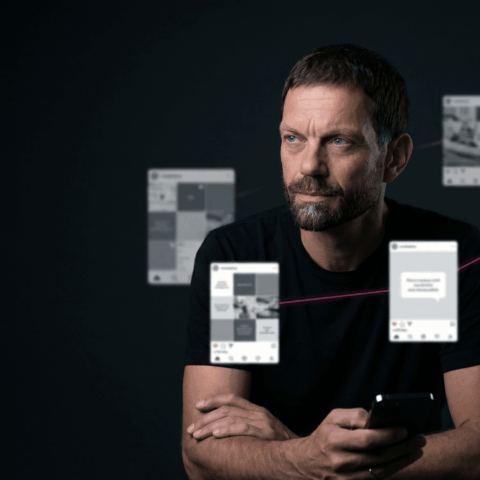 Josip trägt ein schwarzes T-Shirt, hält ein Smartphone in der Hand und blickt nach rechts, umgeben von schwebenden Social-Media-Beiträgen